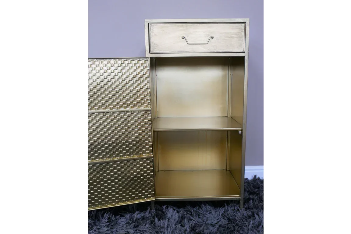 Gold metal storage cabinet with textured door, open shelves and top drawer, on dark rug