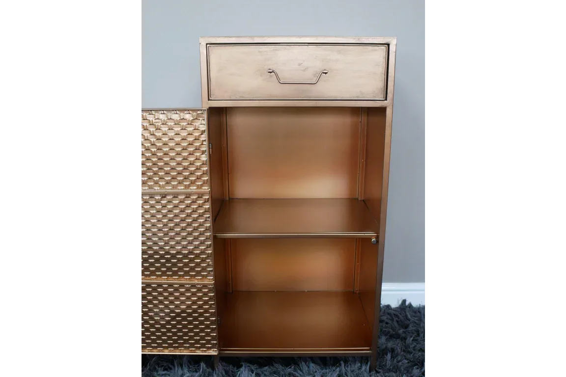 Gold metal storage cabinet with open shelves and drawer, textured door partially visible