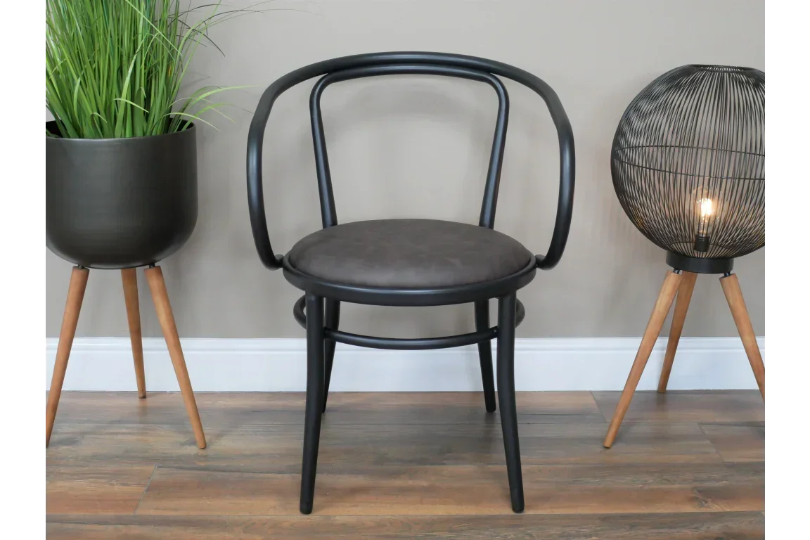 Black modern dining chair with round faux leather seat and curved backrest on wooden floor