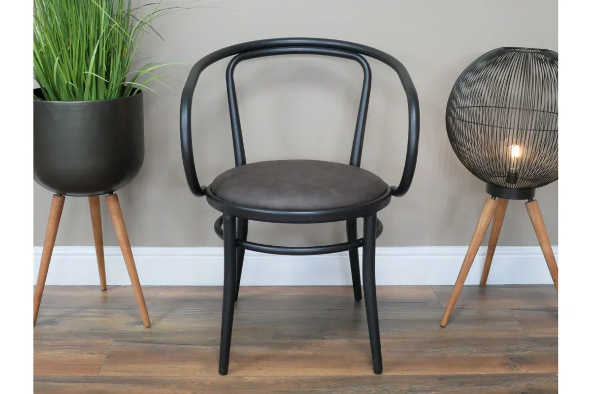 Black accent chair with curved back and padded seat, styled between plant stand and tripod lamp