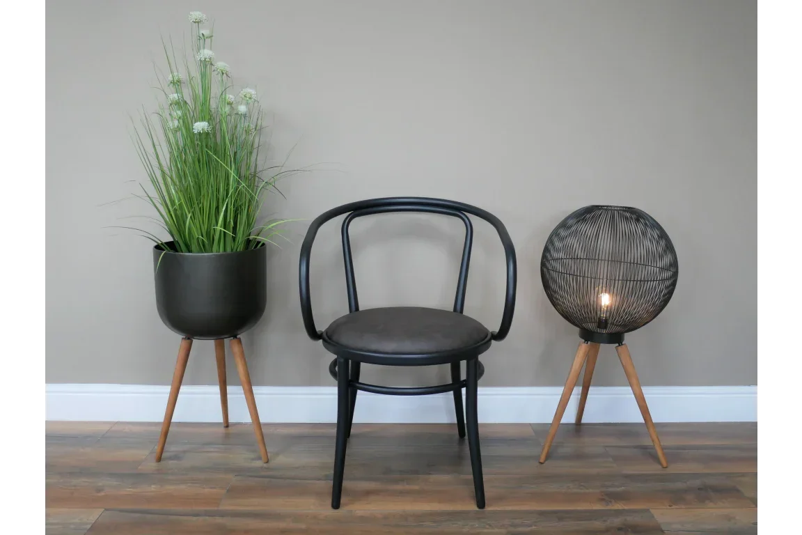 Black accent chair with curved backrest between tripod planter and black wire floor lamp