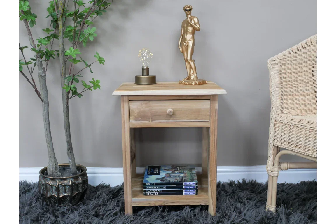 Wooden bedside table with drawer, shelf holding books, lamp and statue on top