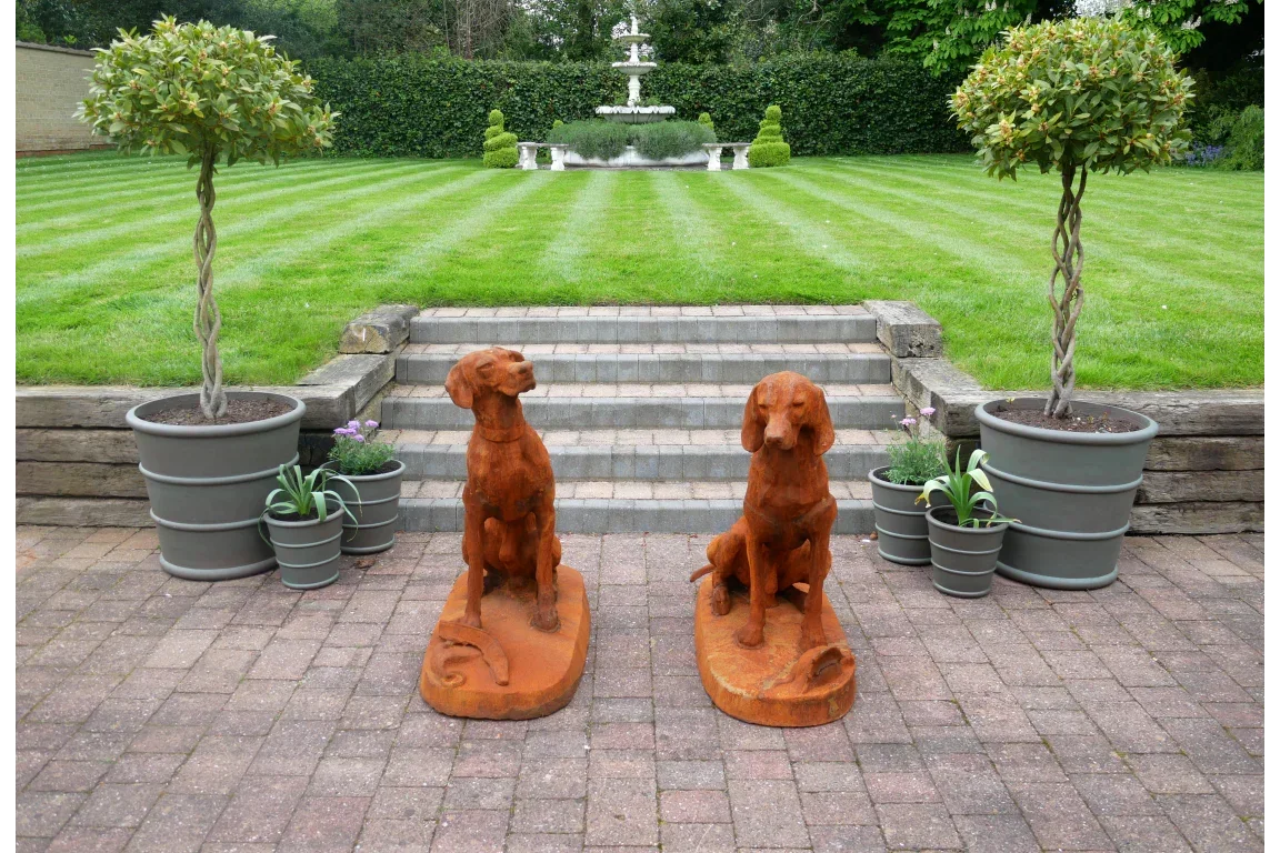 Pair of rusted metal dog garden statues with potted plants on brick patio