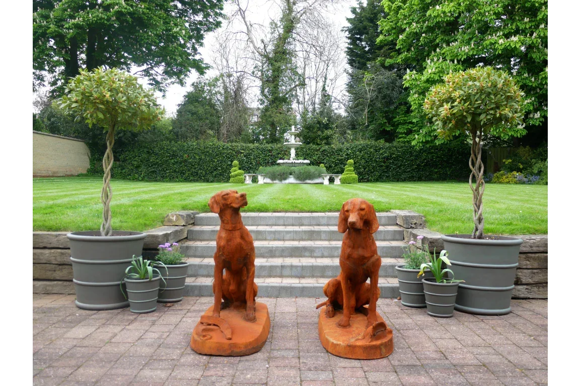 Pair of rust-effect dog statues on patio with potted trees and garden steps