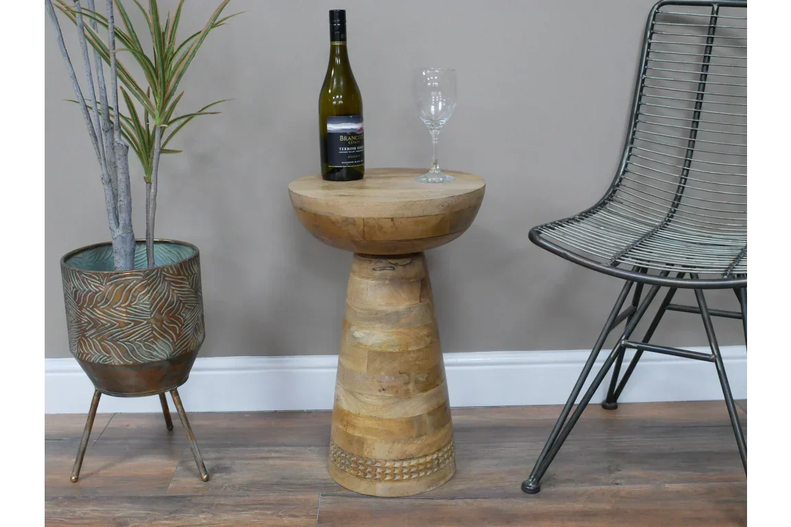 Round mango wood side table with bottle and glass beside metal chair and plant pot