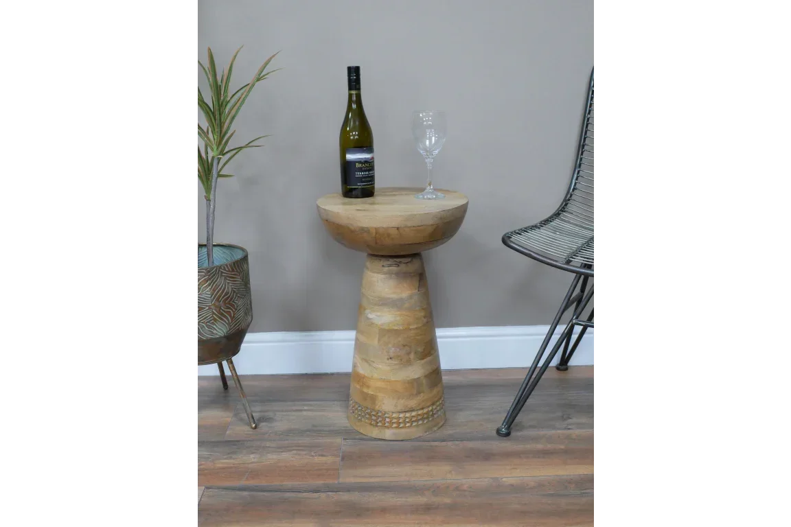Wooden side table with bottle and glass beside metal chair and plant on wooden floor