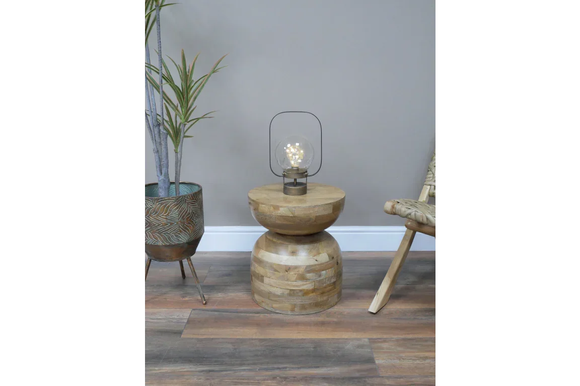 Round wooden side table with modern lamp, next to potted plant and woven chair