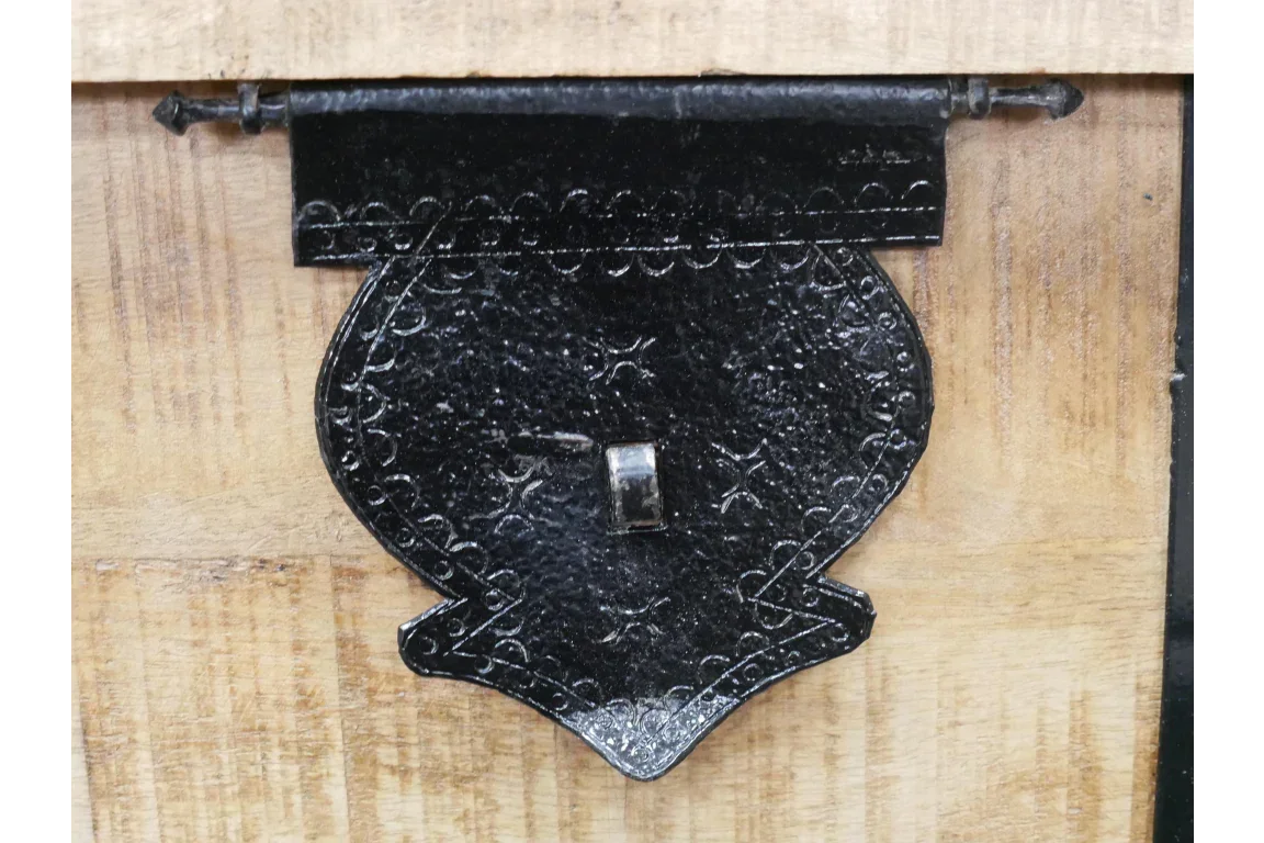 Black metal latch on natural wood furniture drawer front, close-up view