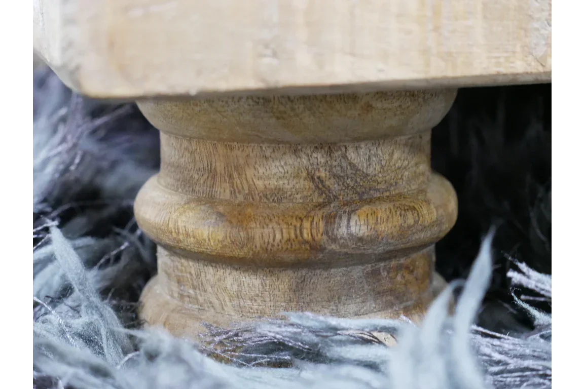 Close view of carved wooden furniture leg on textured grey rug