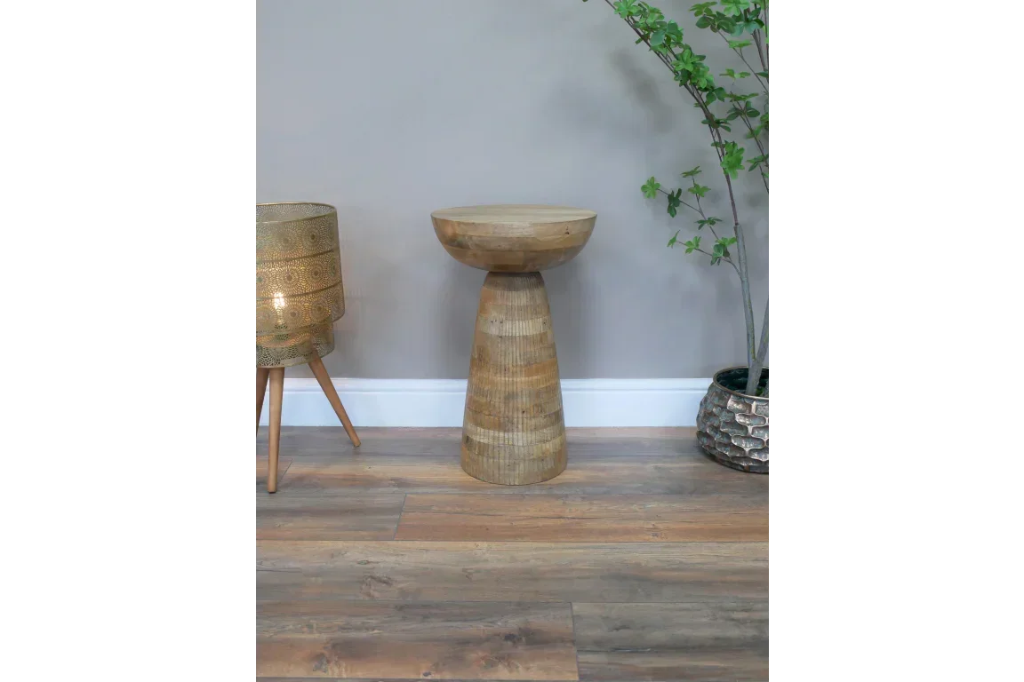 Round wooden side table with natural finish in living room next to plant and gold lamp