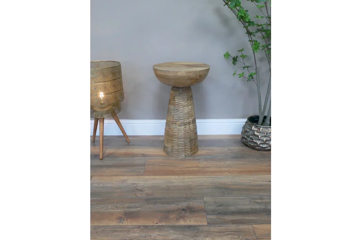 Solid wood side table with textured base on wooden floor beside lamp and potted plant