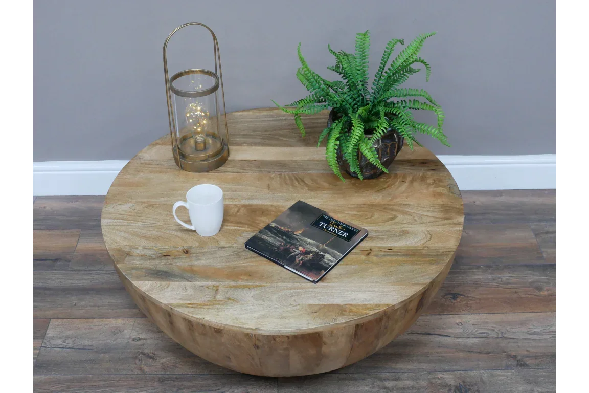 Round solid wood coffee table with potted plant, lantern, mug, and book on wood floor
