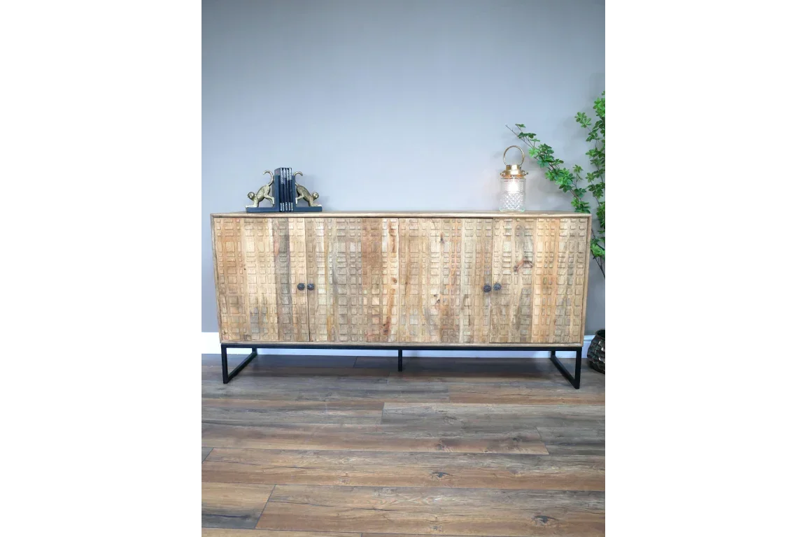 Carved wood sideboard with black metal legs against a grey wall, books and vase on top