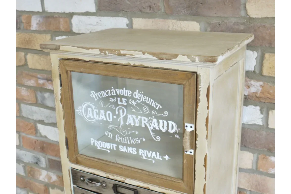 Distressed cream wood cabinet with glass door and vintage French print, against brick wall