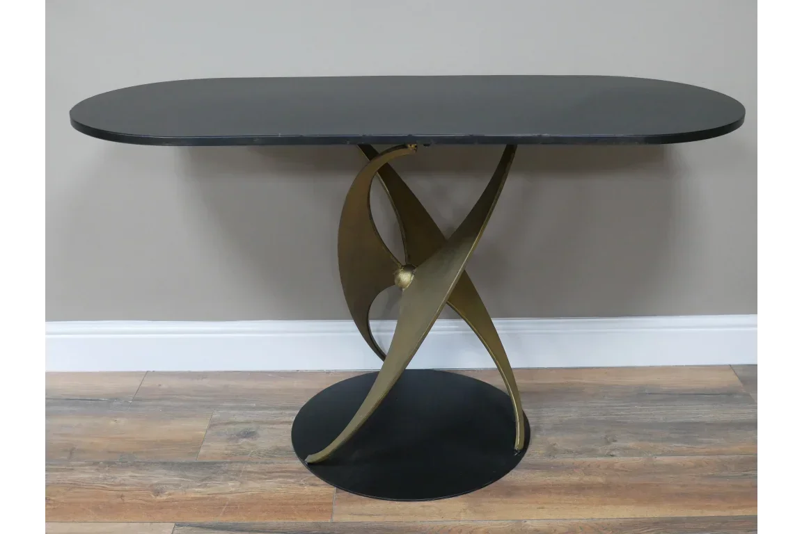 Modern console table with black oval top and sculpted gold metal base on wood floor