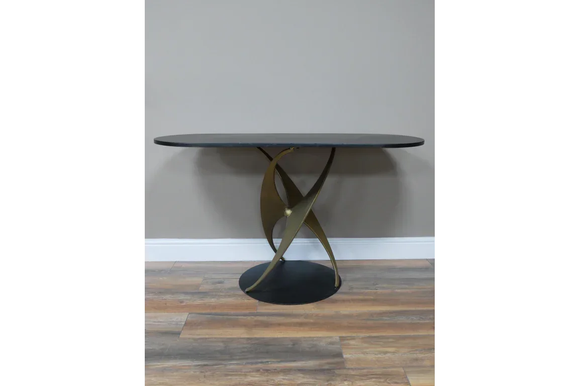 Modern dining table with black oval top and sculptural gold metal base on wood floor