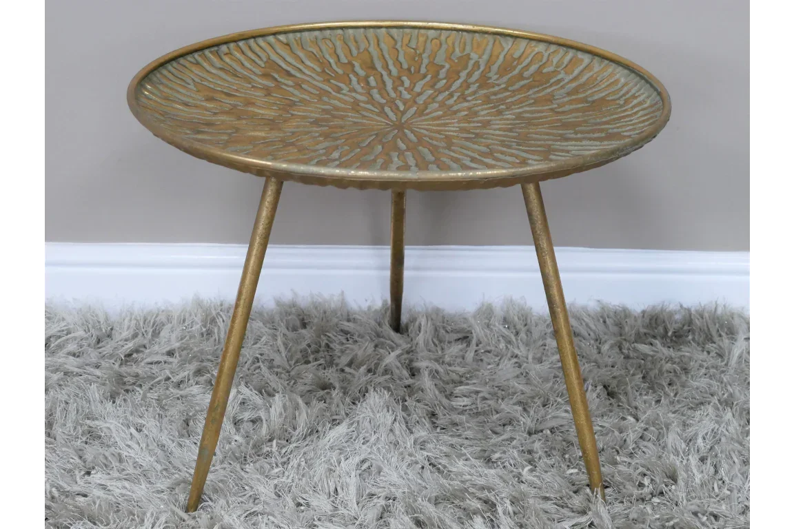 Gold metal side table with textured top and three legs on grey shaggy rug