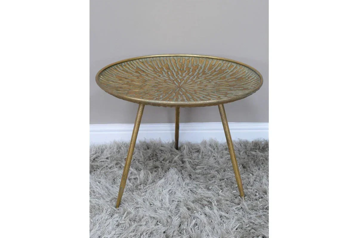 Round gold metal side table with etched top and tripod legs on grey shaggy rug