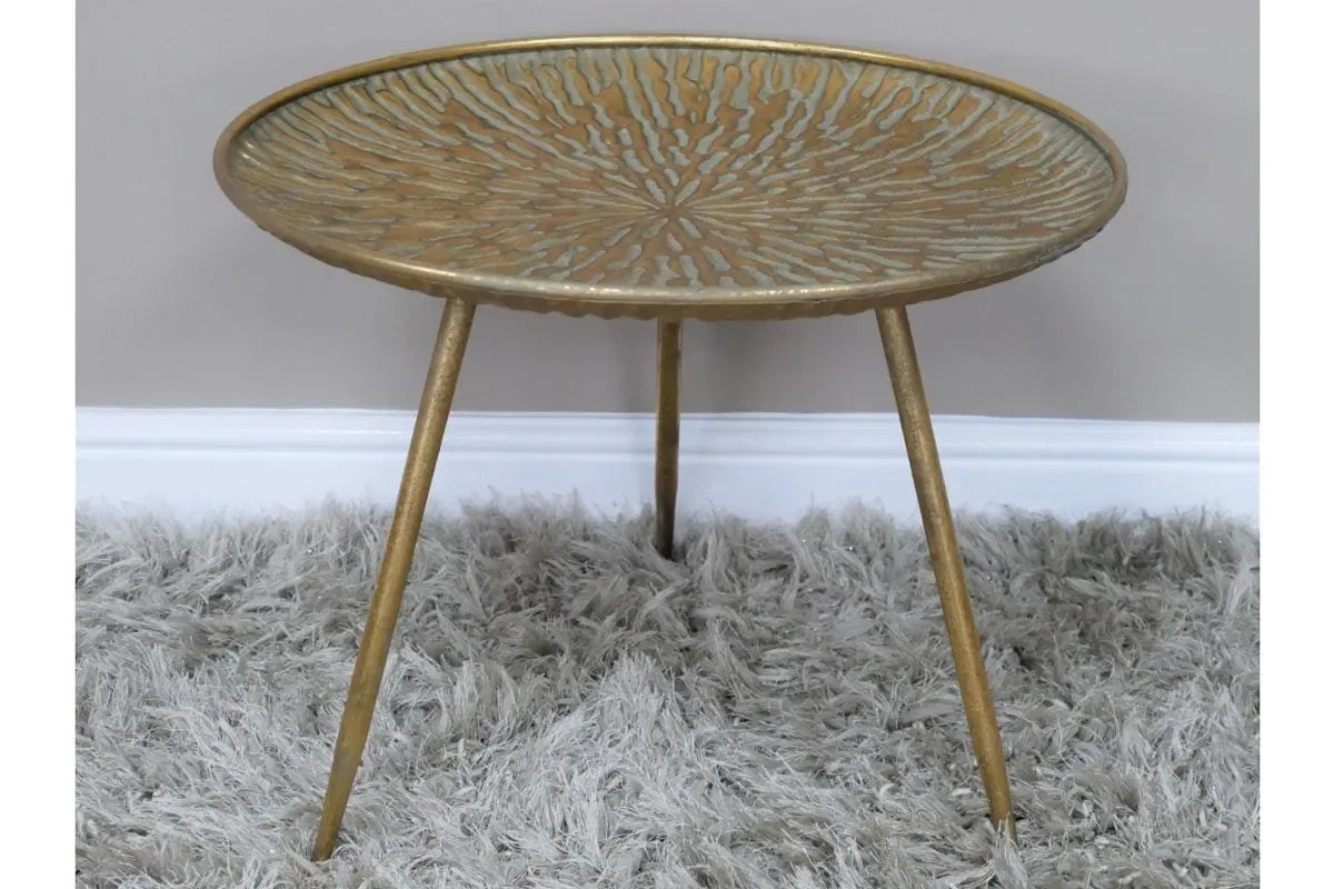Gold metal side table with textured top and tripod legs on a grey shaggy rug