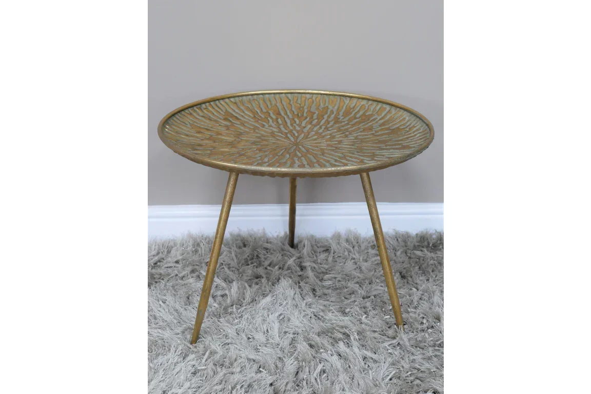 Gold metal side table with textured top and three legs on a grey shaggy rug