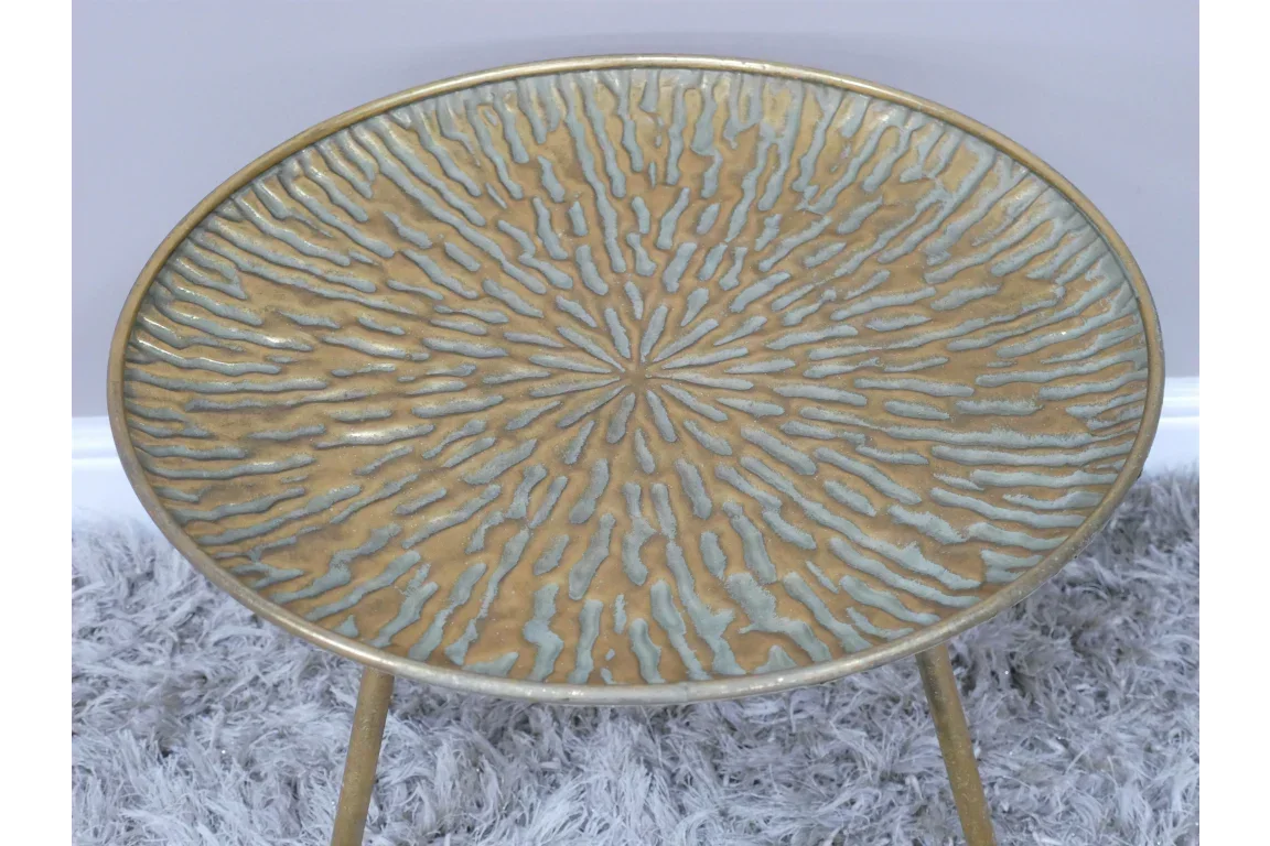 Round gold metal side table with textured sunburst pattern on top, placed on grey rug