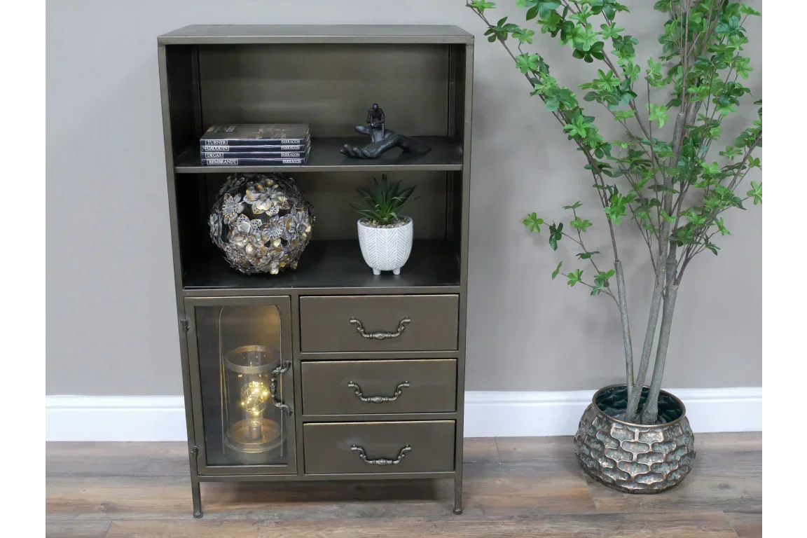 Metal display cabinet with three drawers, shelf decor and side glass door, next to faux plant