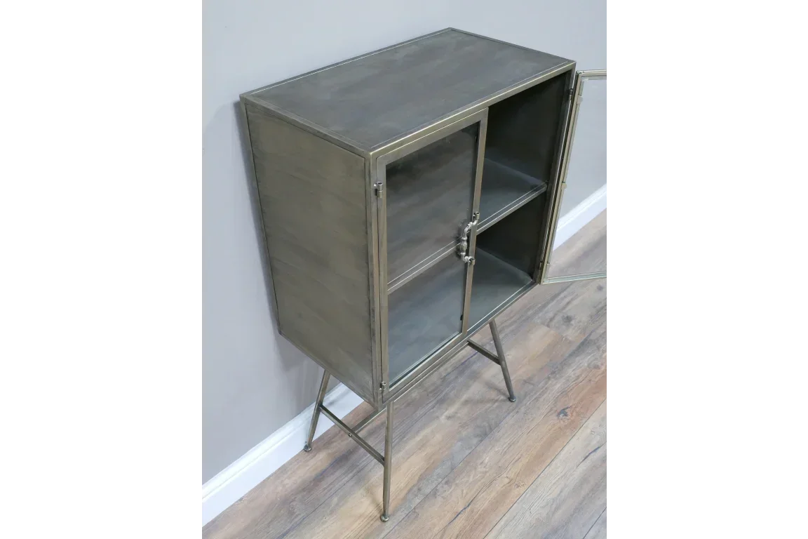 Metal display cabinet with glass doors and shelf on slim legs, shown against a wall