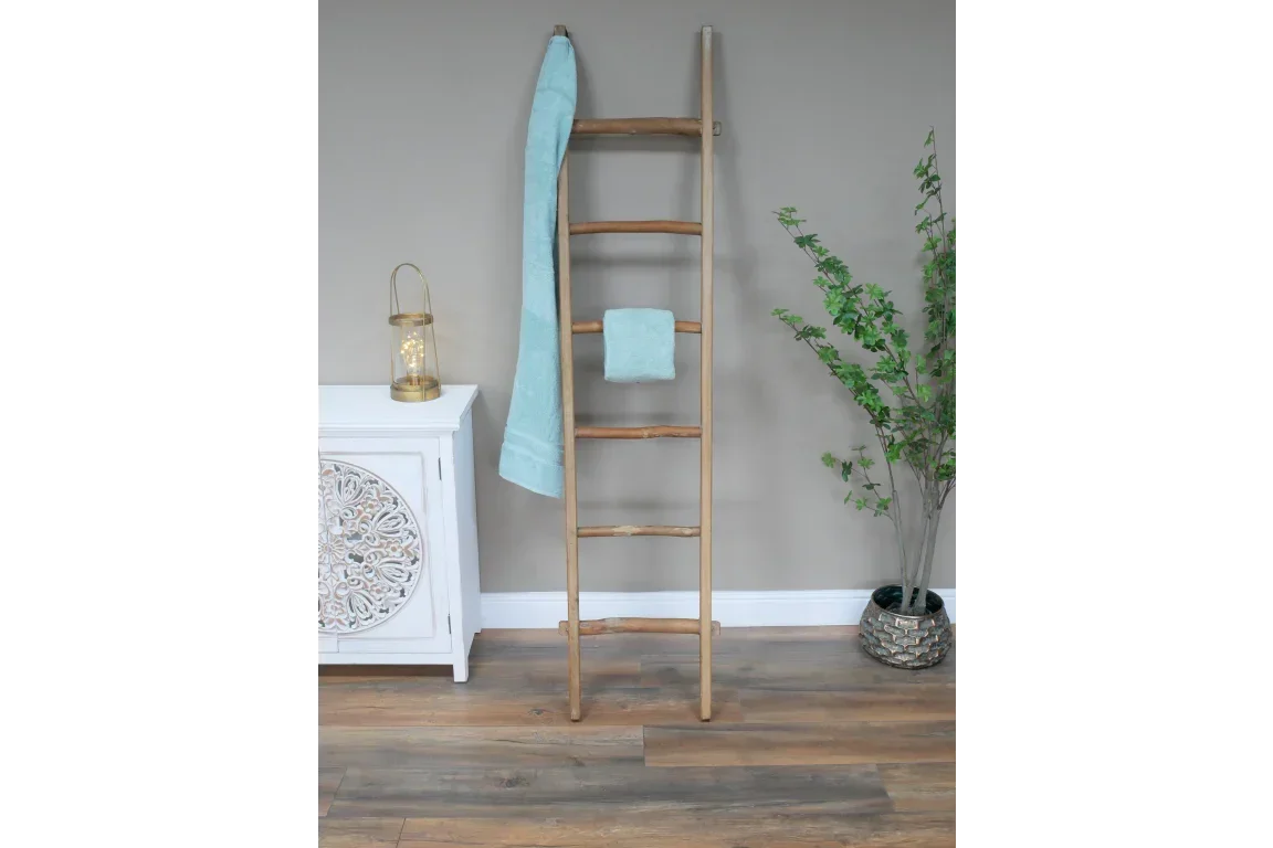 Wooden towel ladder with two blue towels in modern room with decorative cabinet and plant