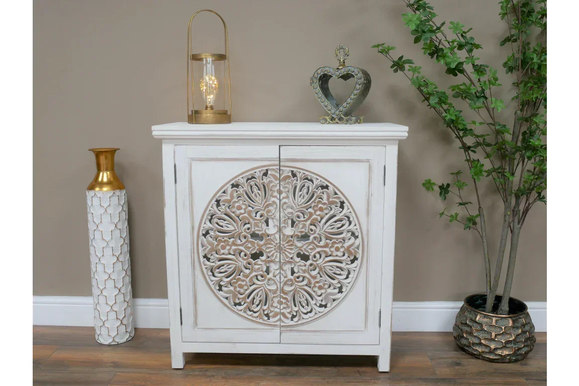 White carved wooden cabinet with ornate round floral design, styled with decor accents