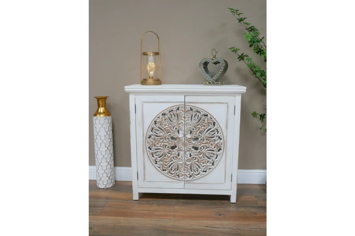 White wooden cabinet with ornate carved door detail, styled with decorative vase and lantern