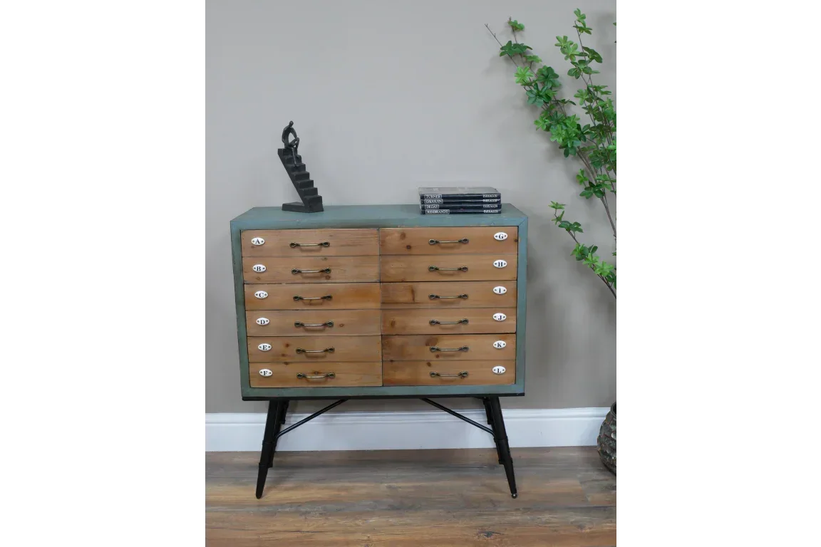Industrial wood chest of drawers with metal handles and black metal legs by a wall with plant