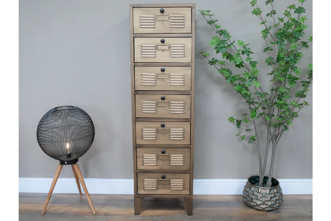 Tall wooden chest of drawers with metal handles beside floor lamp and potted plant