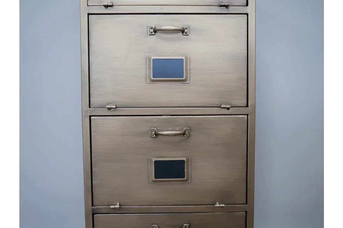Metal filing cabinet with three drawers and label holders against a light blue wall