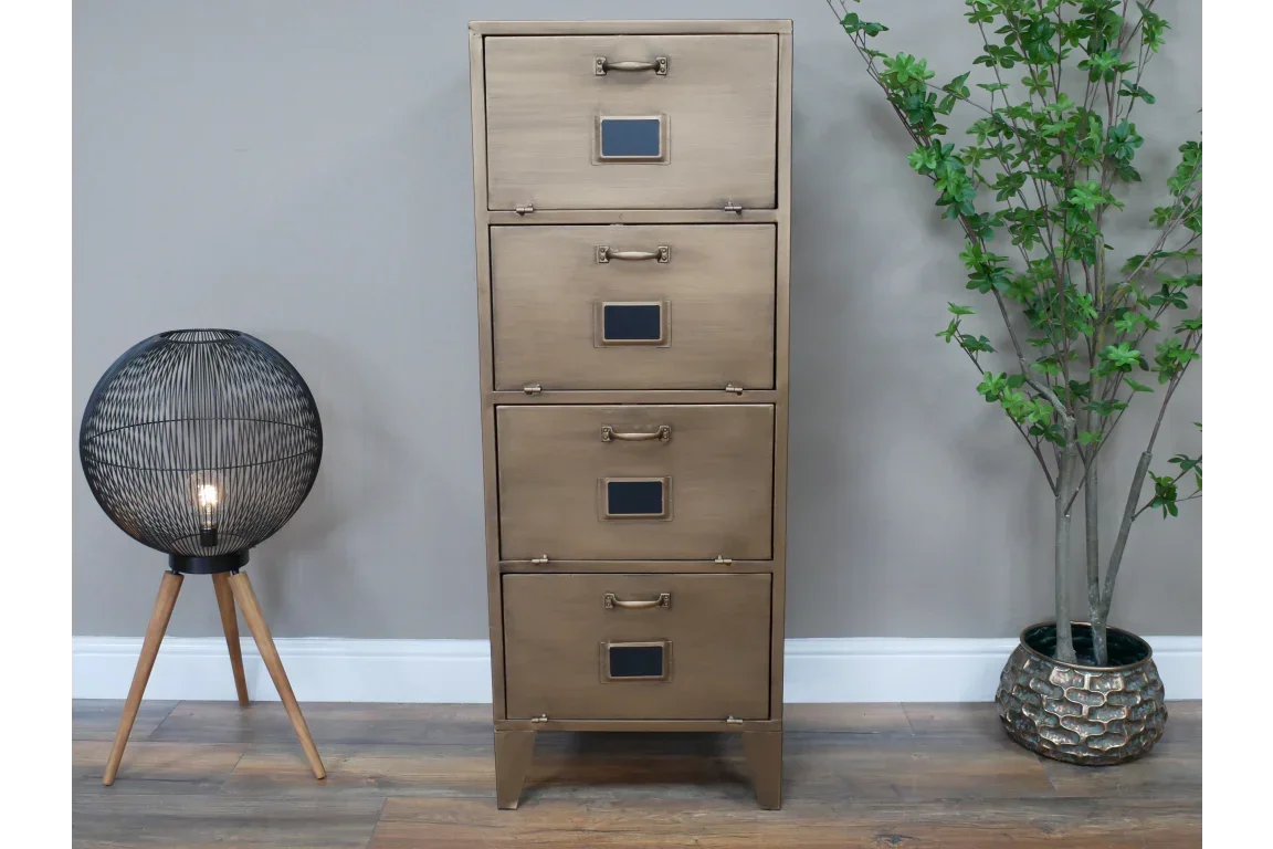 Brass metal filing cabinet with four drawers, standing on wood floor beside lamp and potted plant