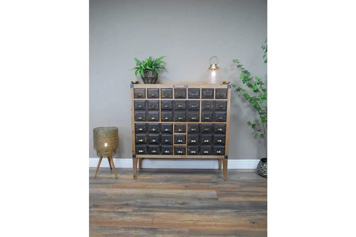 Wooden storage cabinet with multiple drawers, plants and lamp beside on wooden floor