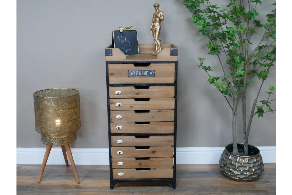 Tall wooden chest of drawers with metal frame, next to gold lamp and potted artificial plant