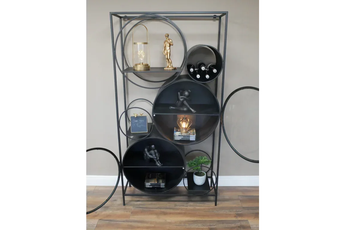 Black metal circular shelving unit with books, sculptures, wine bottles and potted plant