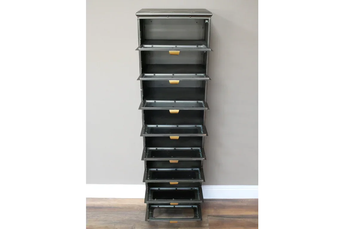 Tall black metal storage unit with eight open drawers and brass handles against wall