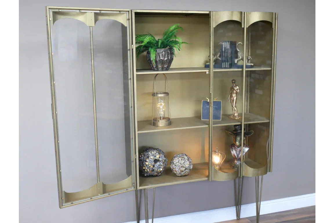 Gold metal display cabinet with glass doors and shelves, decorated with ornaments and books