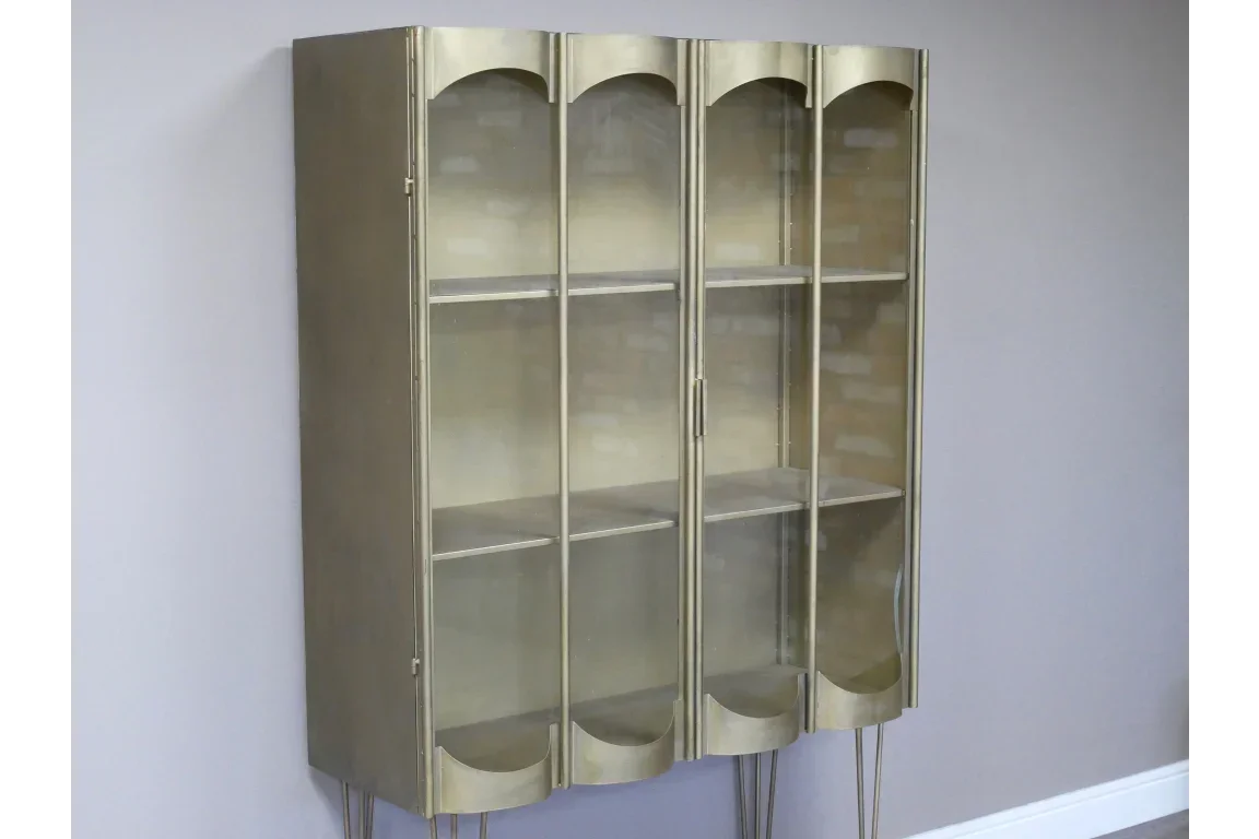 Gold metal display cabinet with glass doors and shelves against a light grey wall