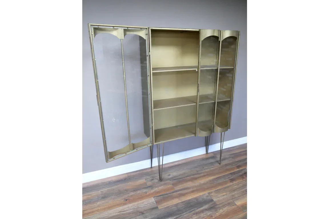 Gold metal display cabinet with glass doors and shelving, shown open on wood floor