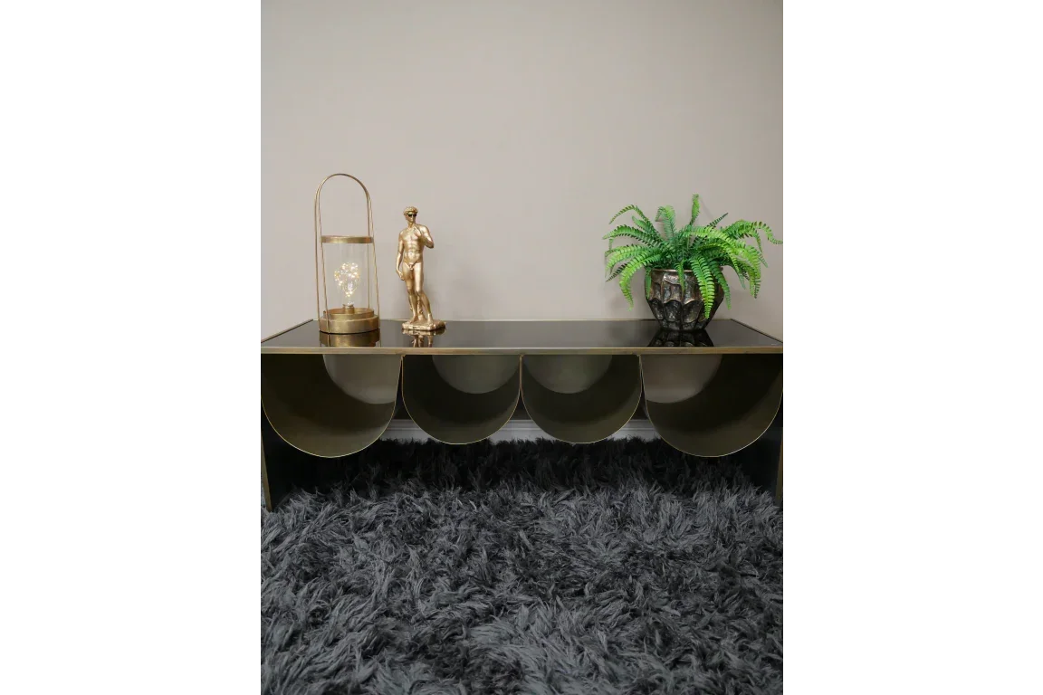 Gold metal console table with decorative statue, lamp, and potted fern on textured rug