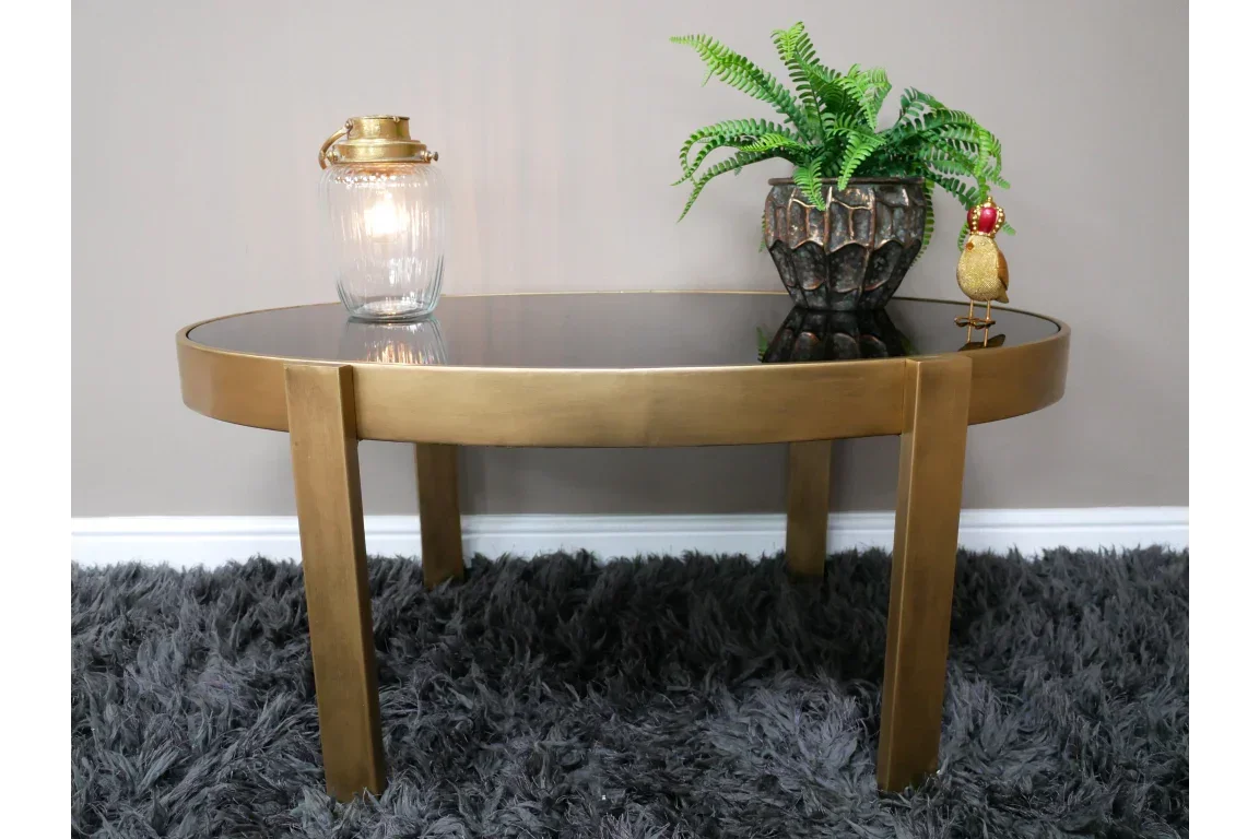Round gold coffee table with black glass top, decor items and potted plant on shaggy rug