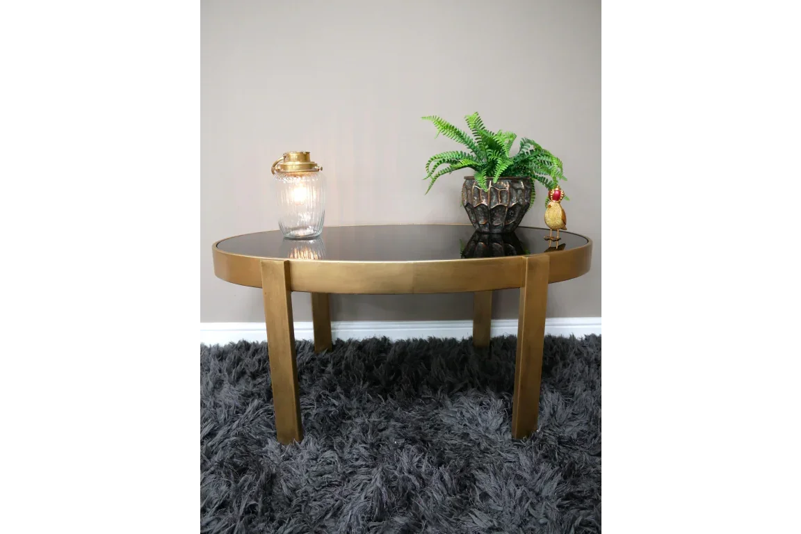 Round gold coffee table with black glass top, plant, and lantern on grey rug