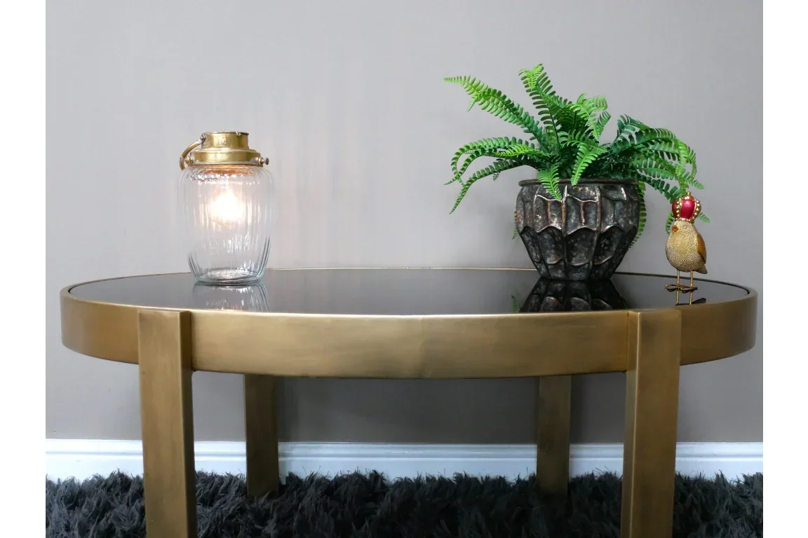 Round gold coffee table with glass top, glass lantern, potted fern, and decorative bird