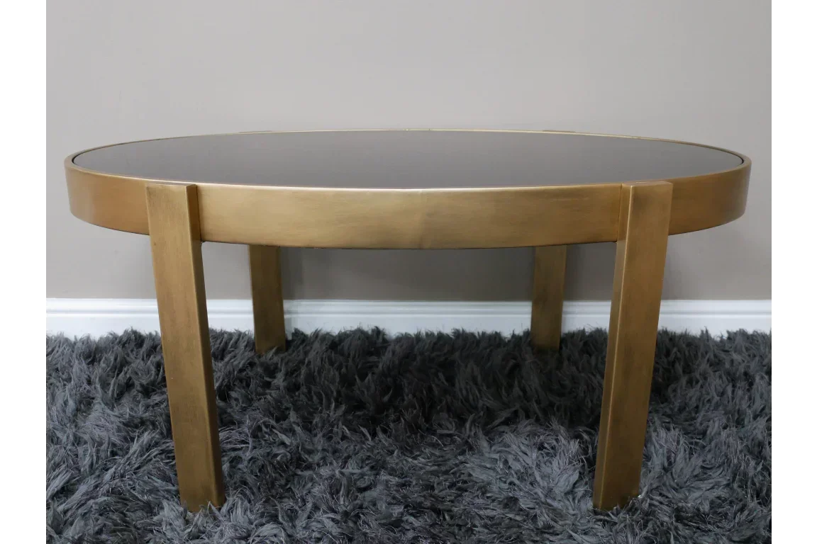 Round gold coffee table with glass top on plush grey rug
