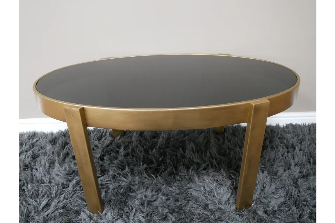 Round gold metal coffee table with black glass top on grey rug