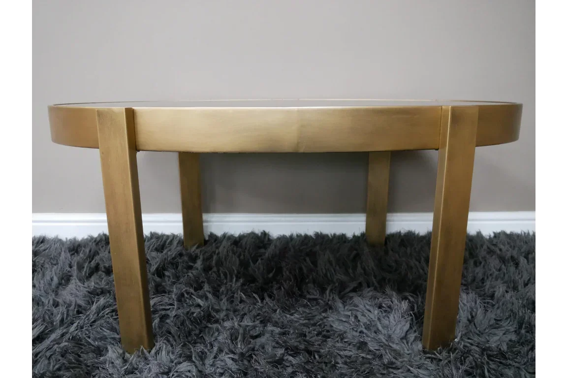 Gold coffee table with metal legs on grey shaggy rug against neutral wall