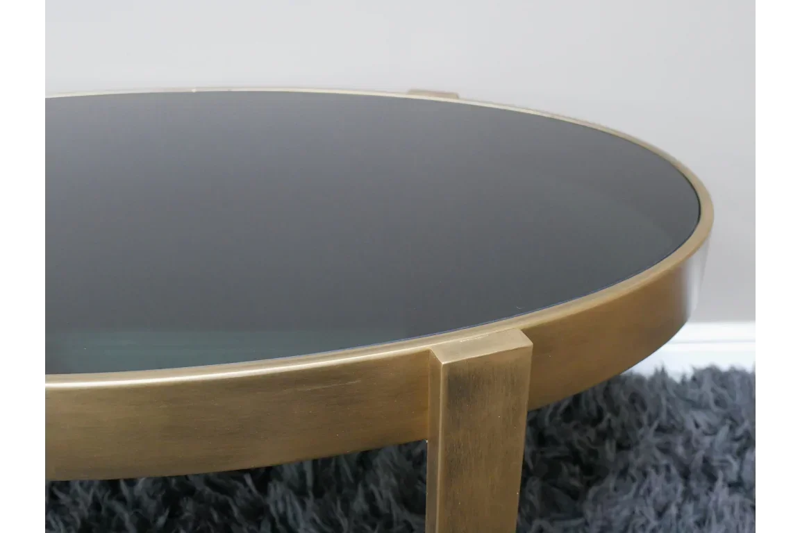 Round glass coffee table with gold metal frame on plush dark rug