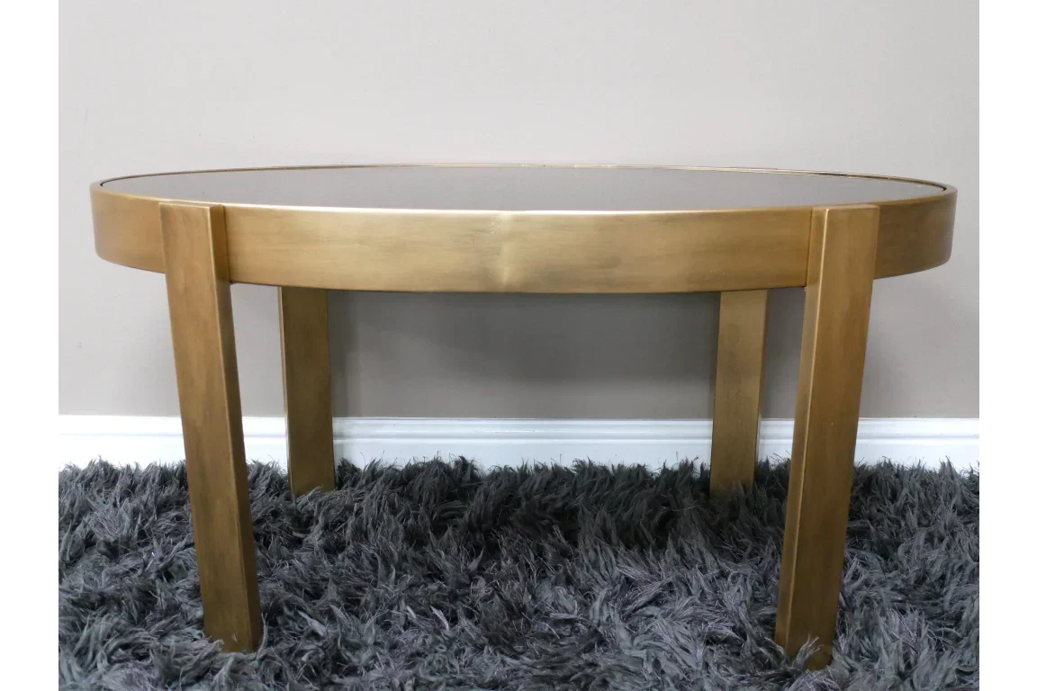 round gold coffee table with glass top and four legs on a grey shaggy rug